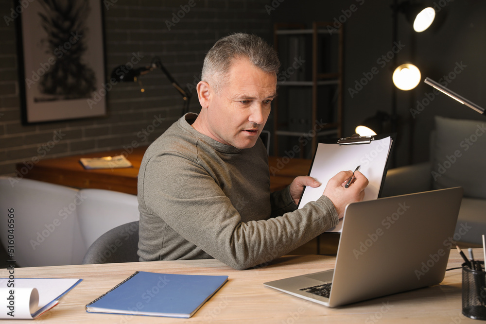 Mature man with laptop video chatting late in evening