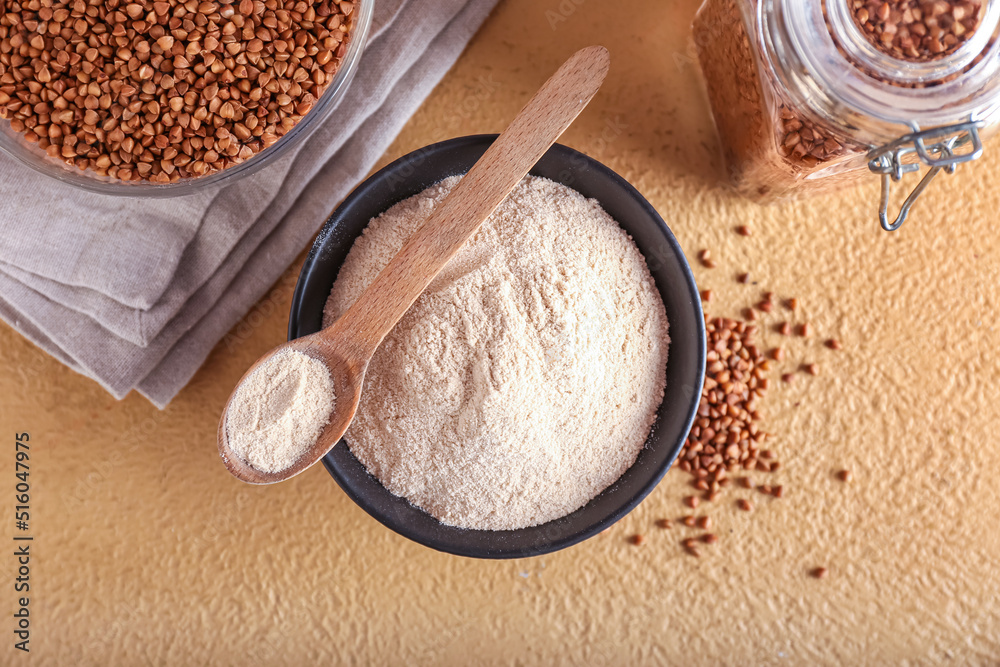 Bowl of flour, spoon and buckwheat grains on beige background