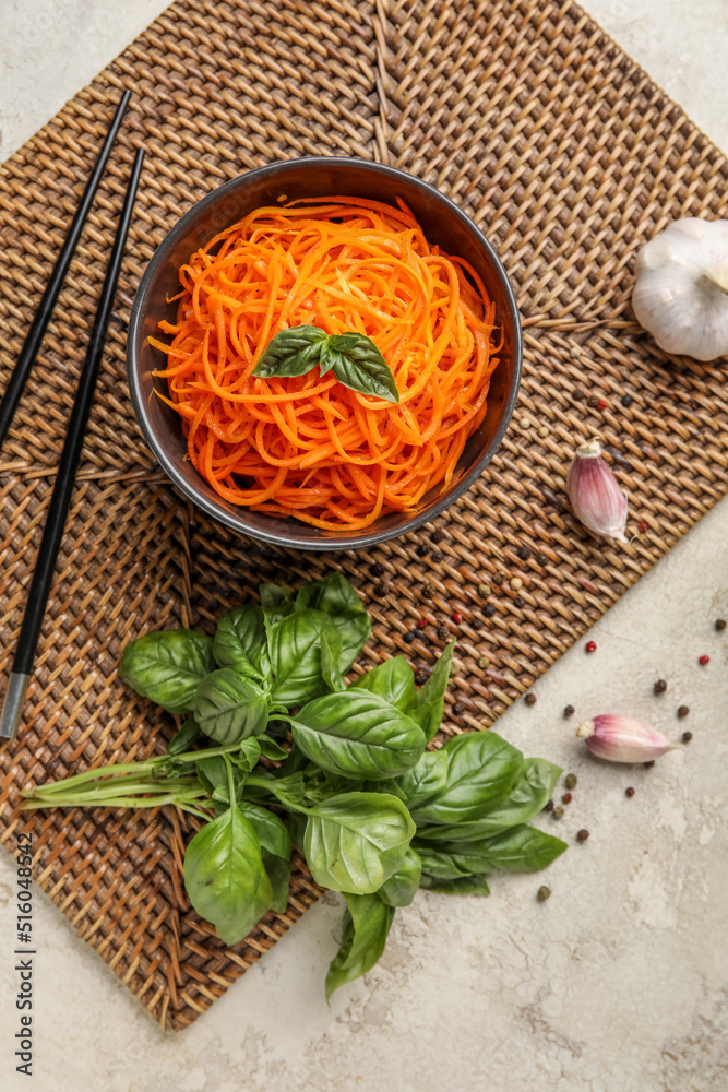 Composition with bowl of tasty korean carrot salad, spices and basil on light background