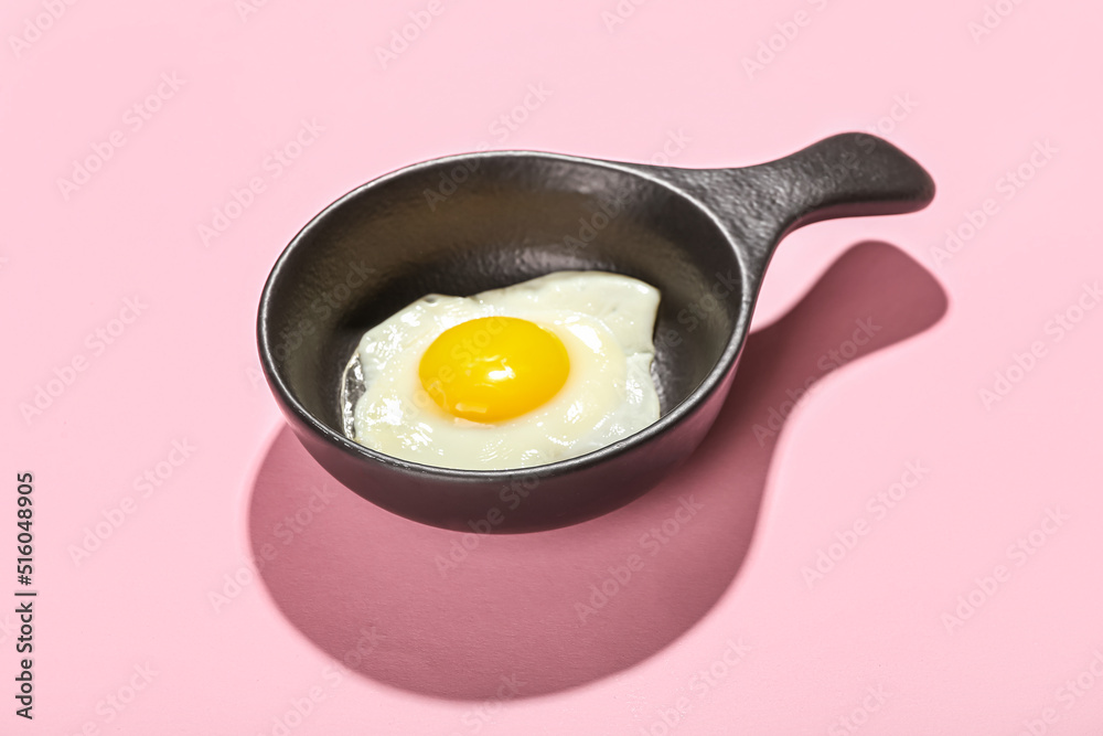 Frying pan with tasty egg on pink background