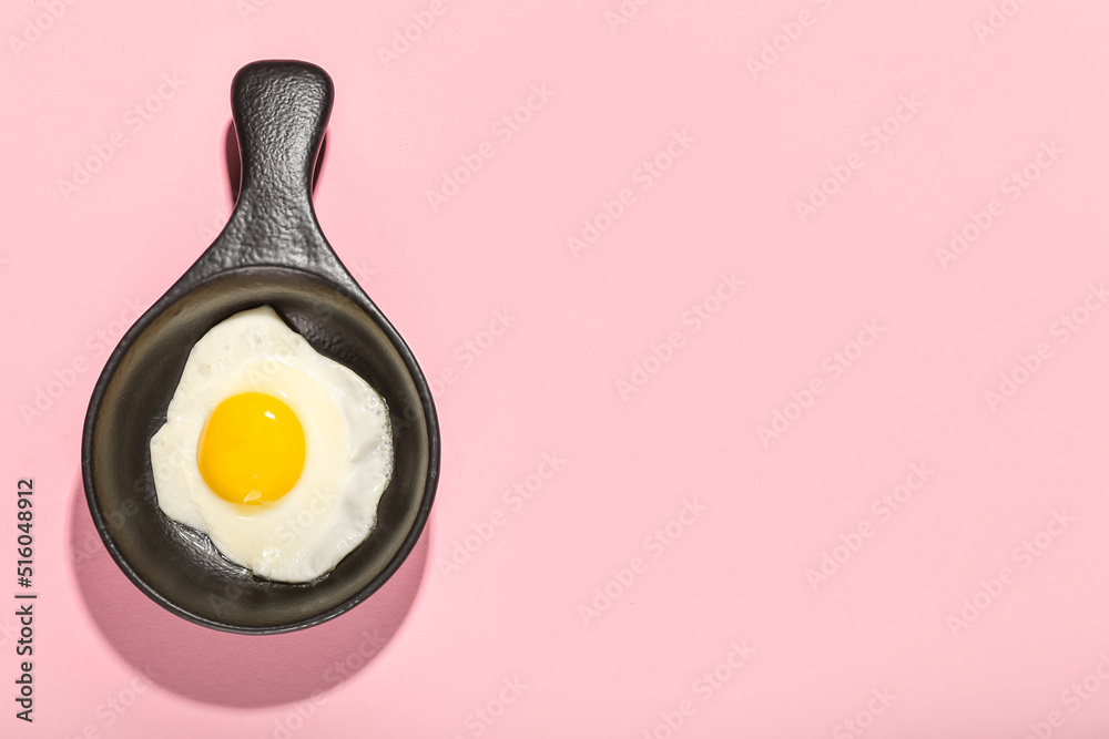 Frying pan with tasty egg on pink background