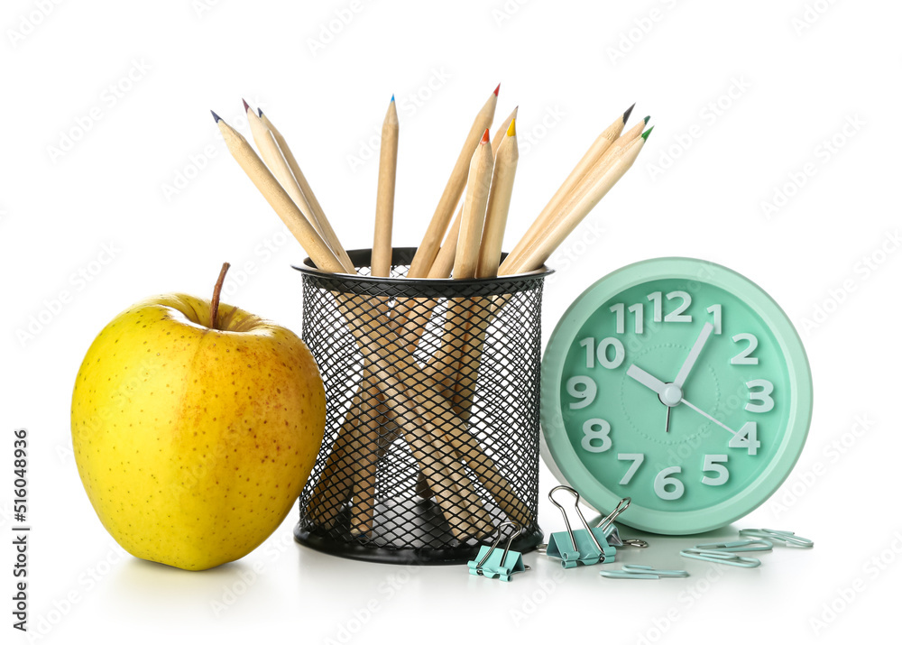 Holder with pencils, paper clips, alarm clock and apple on white background