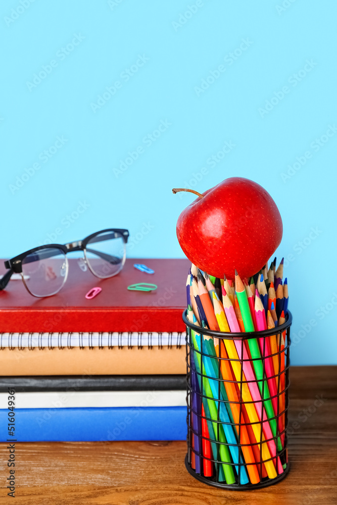 School stationery with apple and eyeglasses on table against blue background