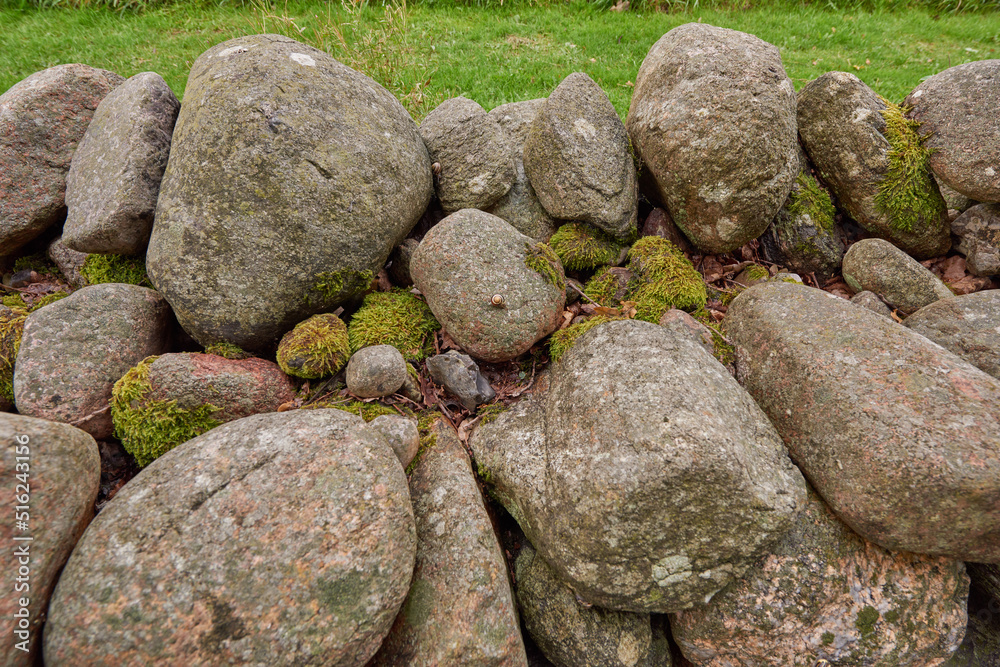 Closeup of a stone wall made of boulders and rocks outside. Background of rustic, rural building and