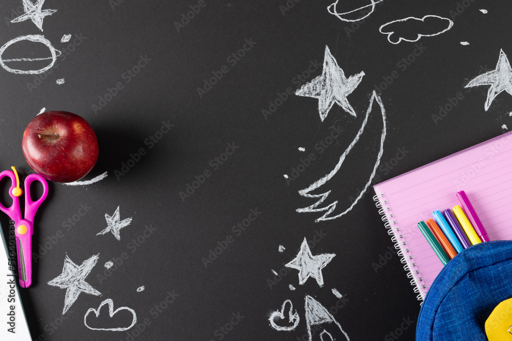 Image of school supplies, apple and notebook over drawings on black board