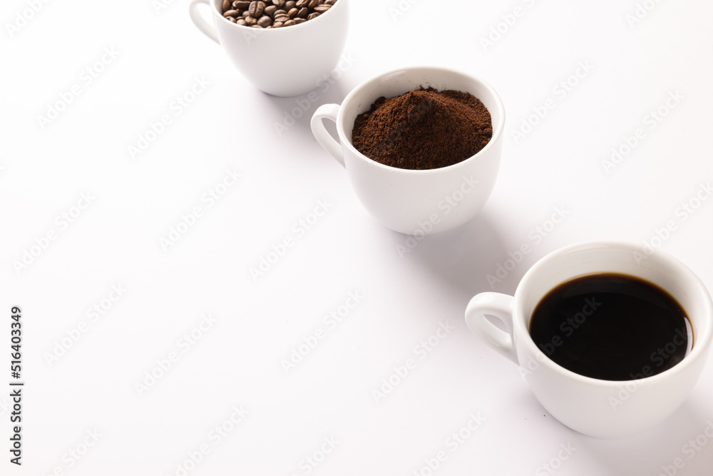 Image of three cups full of ground coffee, coffee beans and coffee on white background