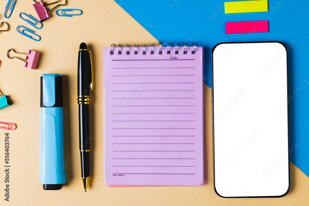 Composition of smartphone with copy space, notebook and school tools on yellow and blue surface