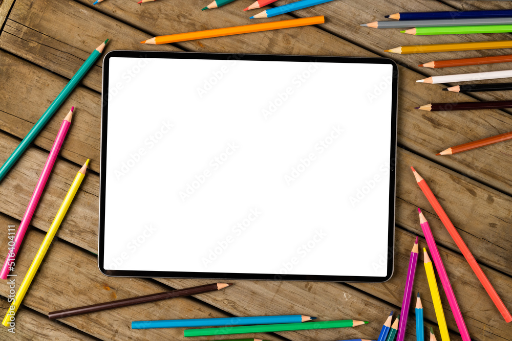 Composition of tablet with copy space and crayons on wooden surface