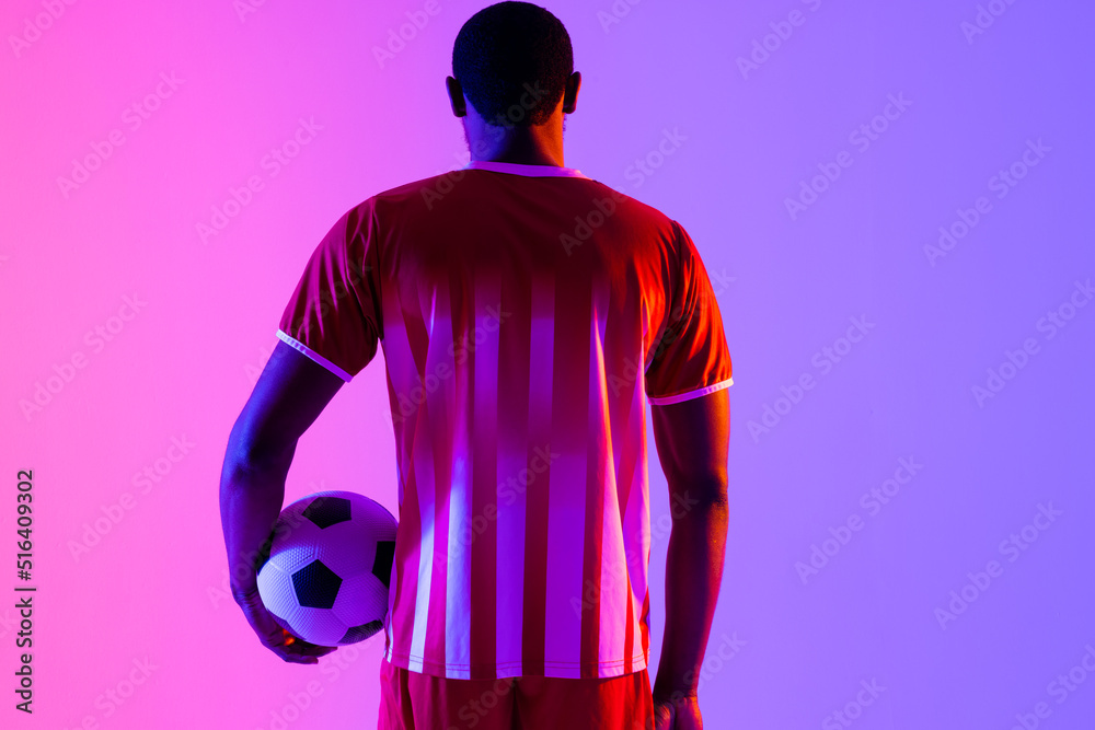 African american male soccer player with football over neon pink lighting