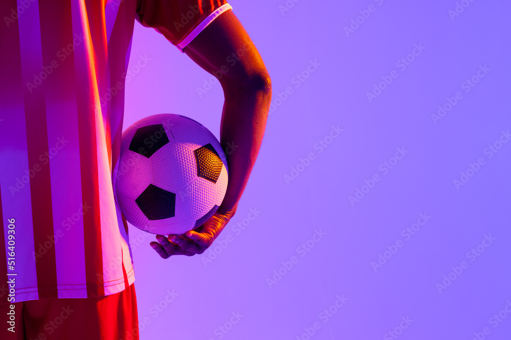 African american male soccer player with football over neon pink lighting