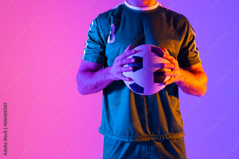 Caucasian male soccer player with football over neon pink lighting