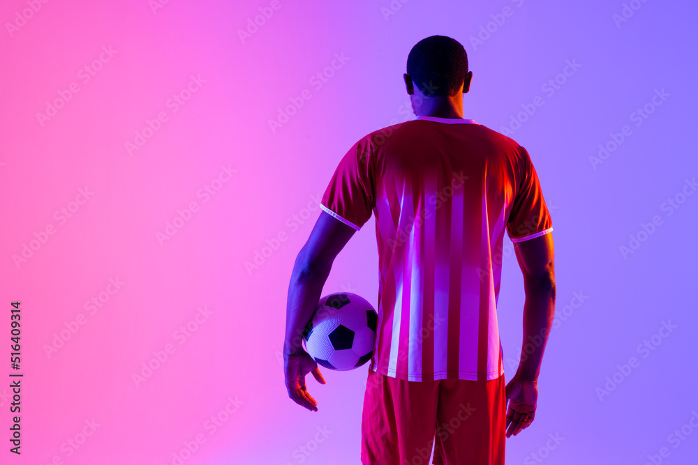 African american male soccer player with football over neon pink lighting