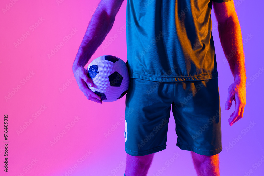 Caucasian male soccer player with football over neon pink lighting