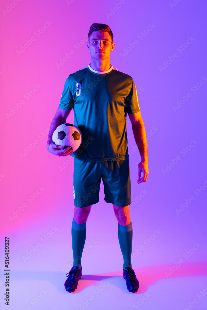 Portrait of caucasian male soccer player with football over neon pink lighting