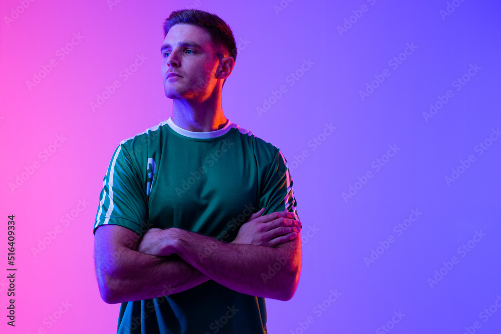 Caucasian male soccer player with arms crossed over neon pink lighting