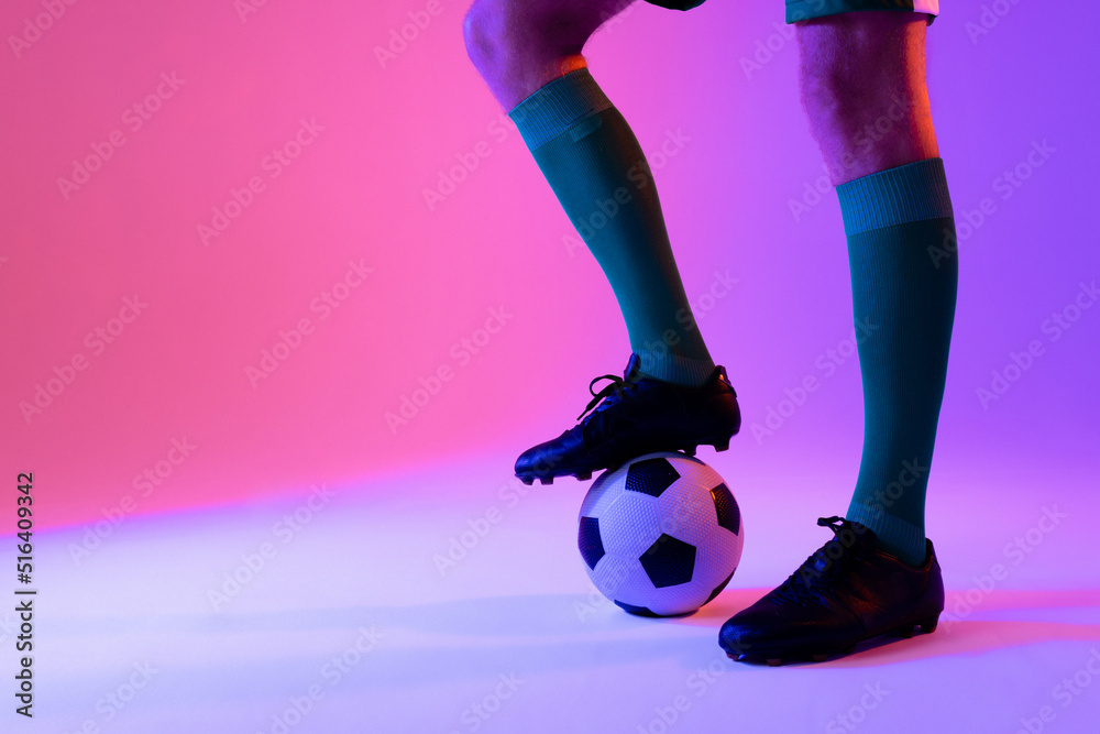 Caucasian male soccer player with football over neon pink lighting