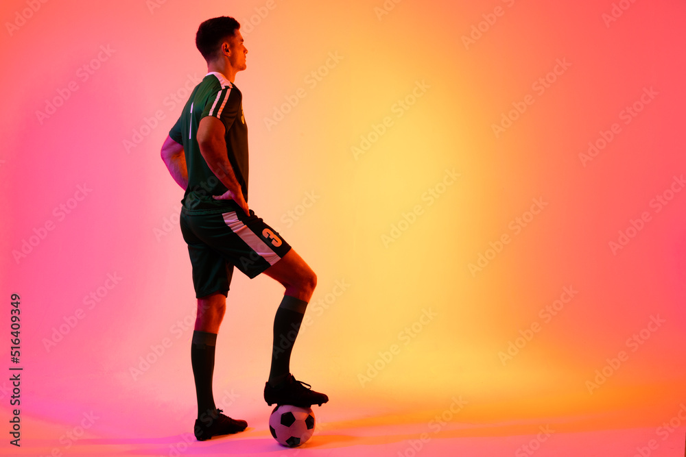 Caucasian male soccer player with football over neon pink lighting