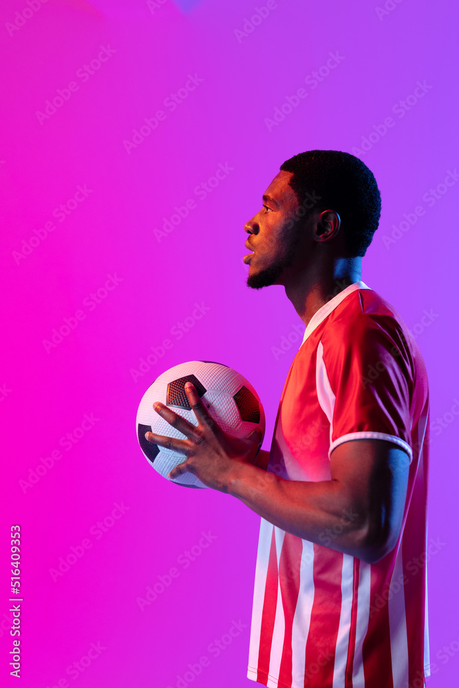 African american male soccer player with football over neon pink lighting