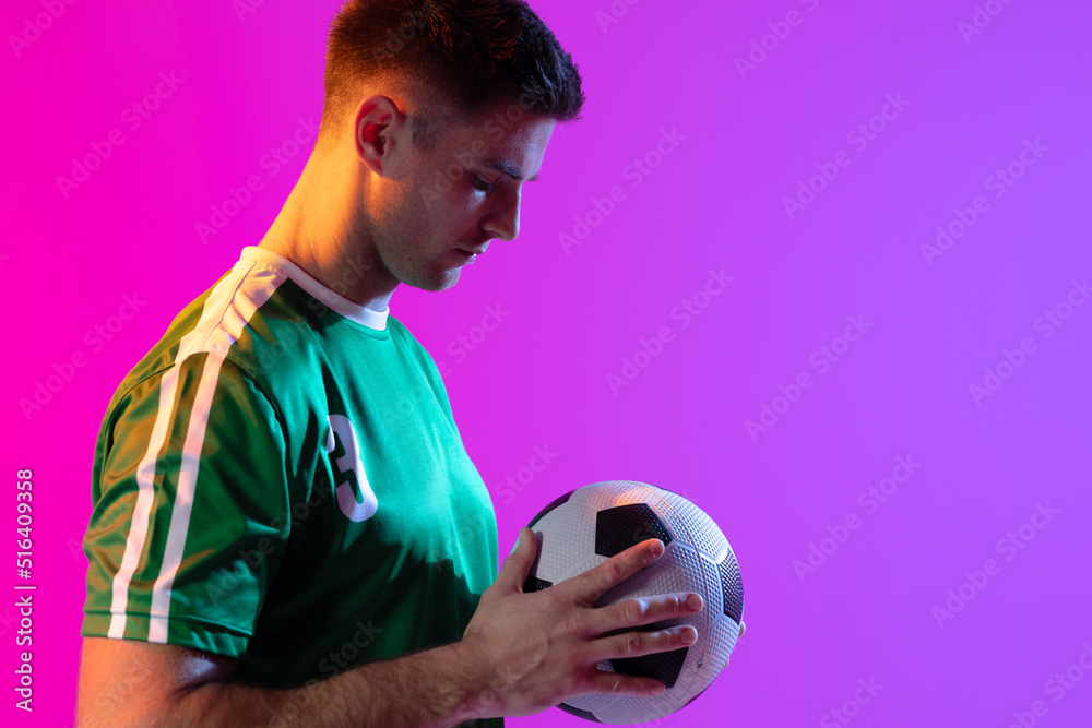 Caucasian male soccer player with football over neon pink lighting