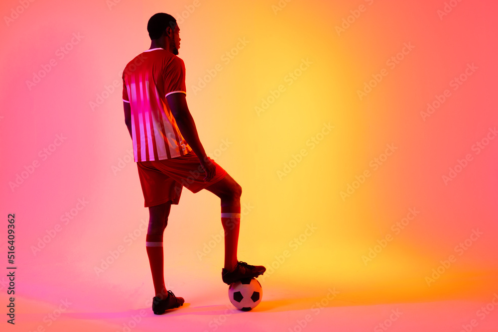 African american male soccer player with football over neon pink lighting