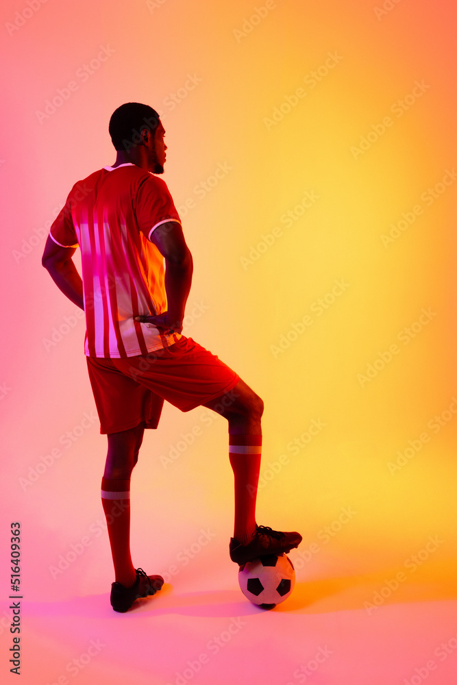 African american male soccer player with football over neon pink lighting