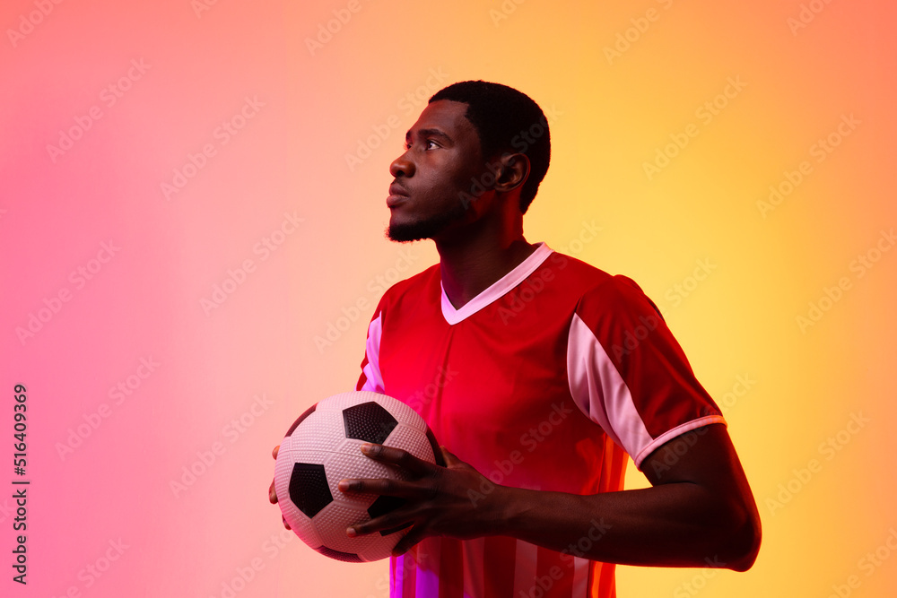 African american male soccer player with football over neon pink lighting