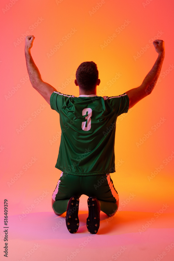 Caucasian male soccer player raising hands over neon pink lighting