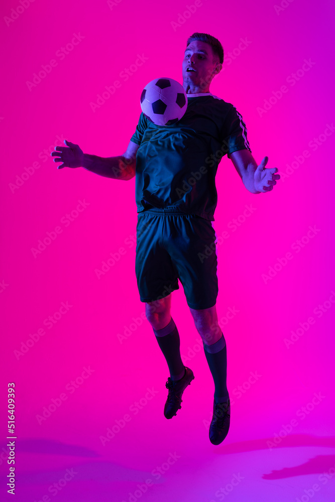 Caucasian male soccer player playing with football over neon pink lighting