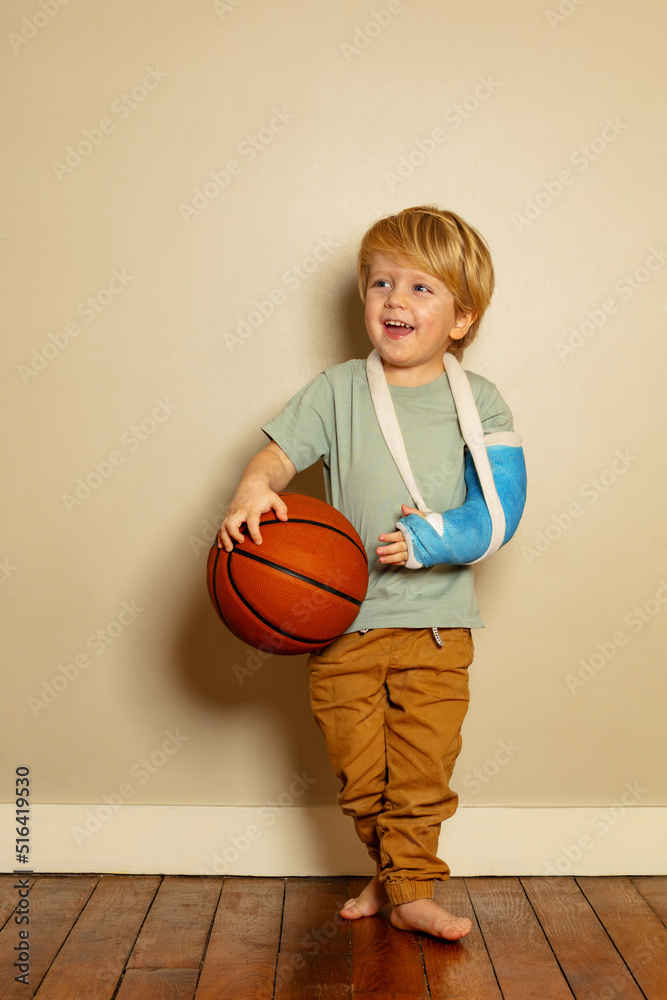 Blond boy hold basketball ball with broken hand in plaster cast