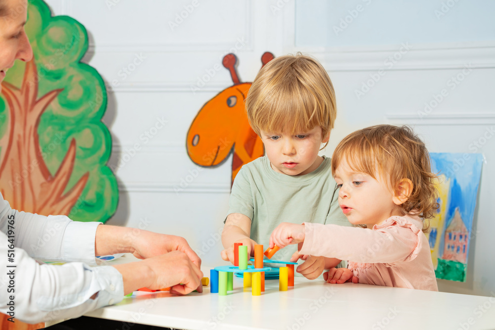 Woman and two little kindergarten kids build tower