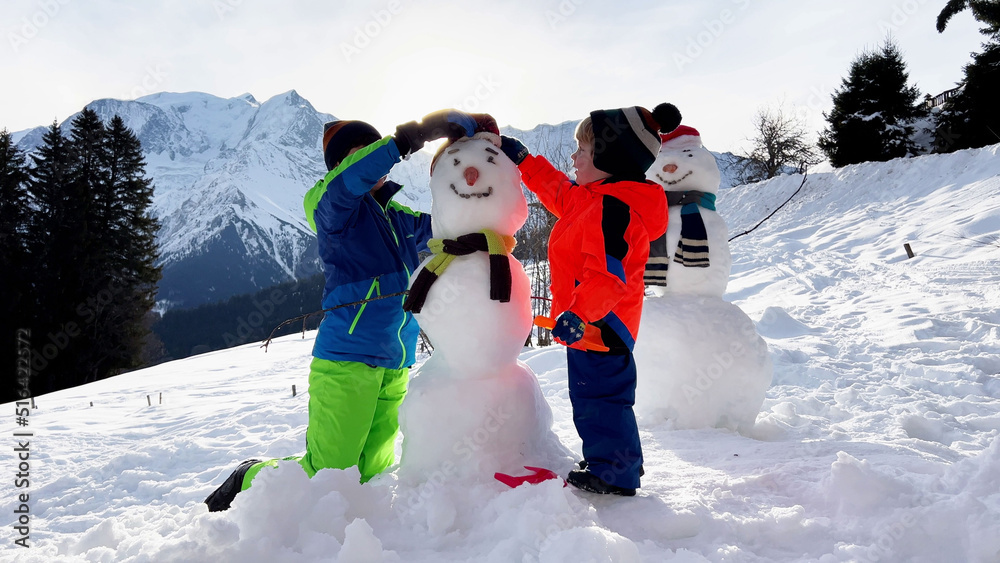 两个男孩一起堆雪人，戴着帽子和围巾