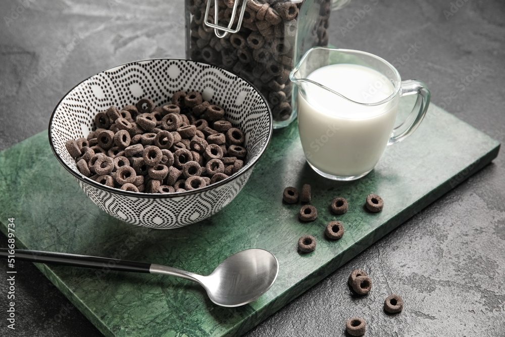 Bowl with tasty cereal rings and gravy boat of milk on dark background