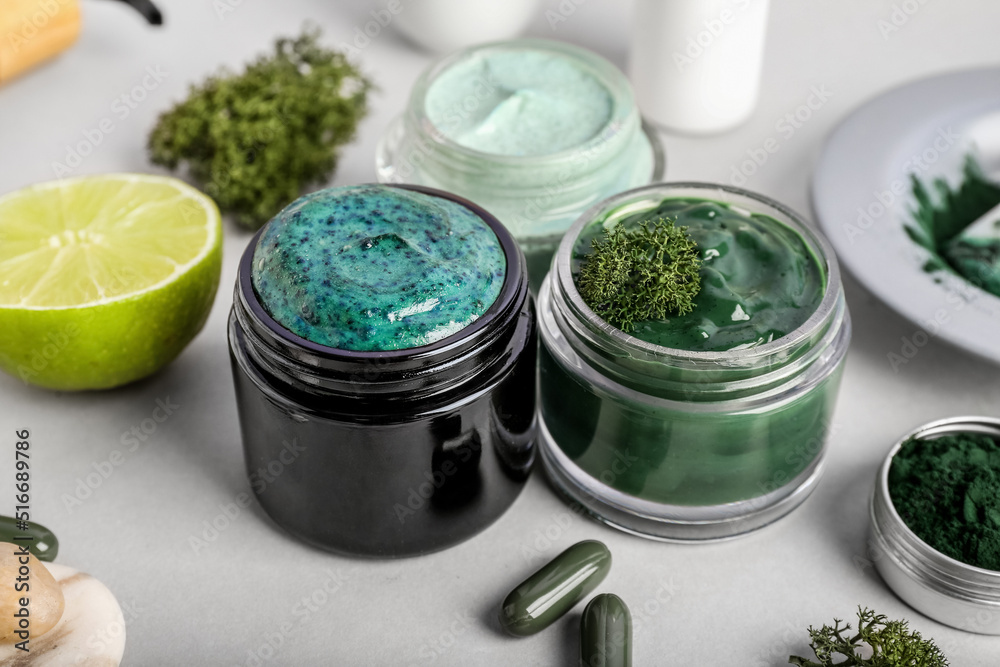 Jars of cosmetics with spirulina extract on light background