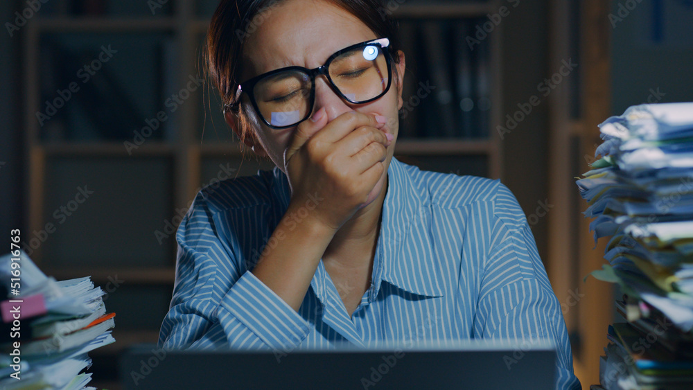 Overworked young Asian office employee yawn during working on laptop computer overtime at night in o