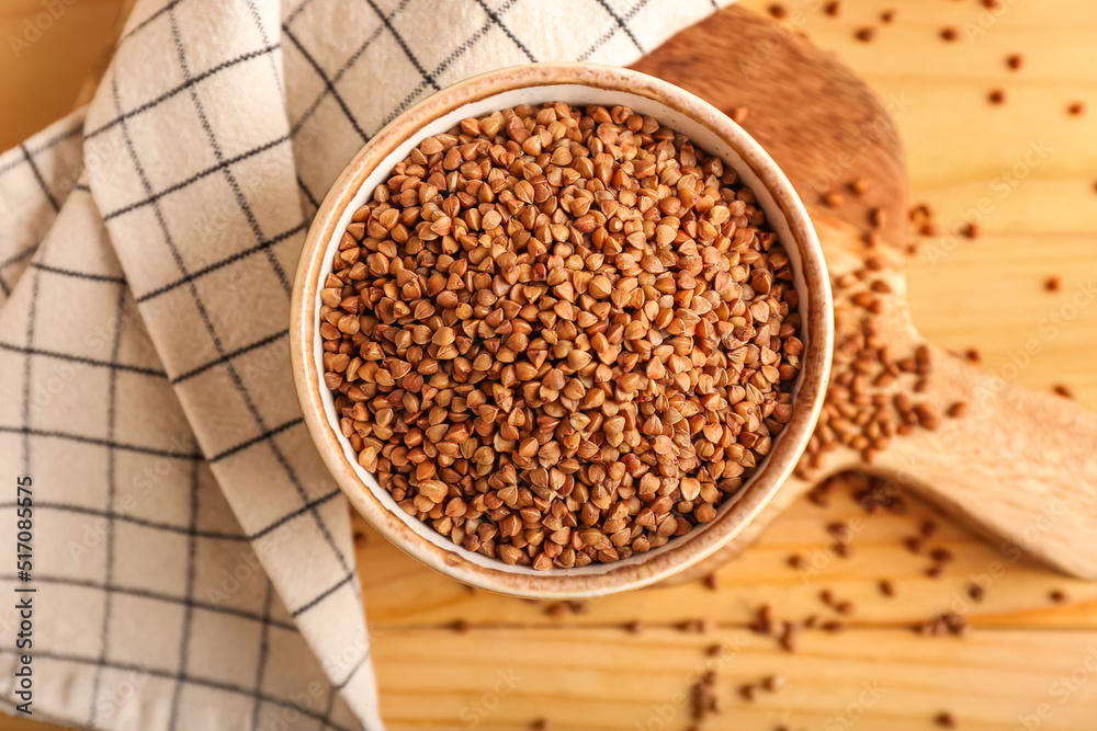 Bowl with buckwheat grains and napkin on wooden table