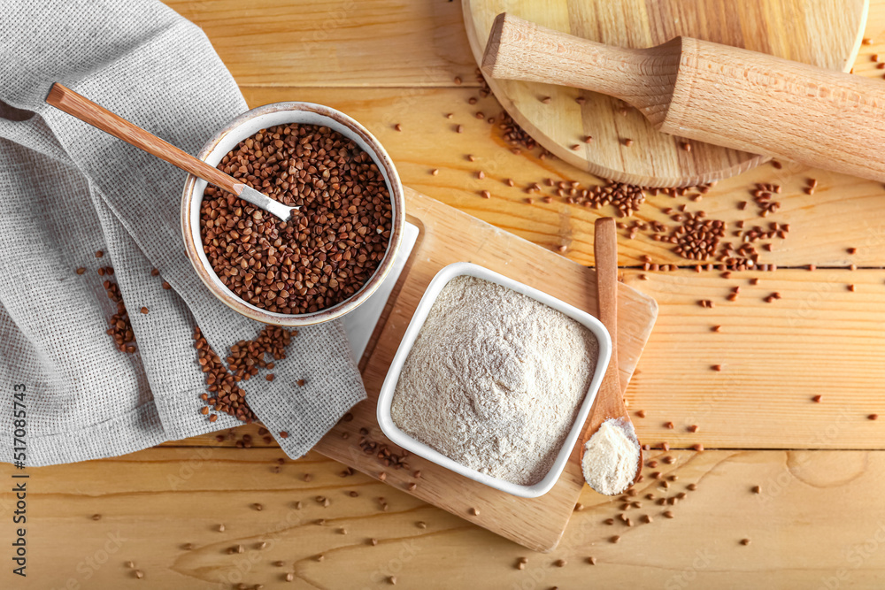 Board with bowls of flour and buckwheat grains on wooden background