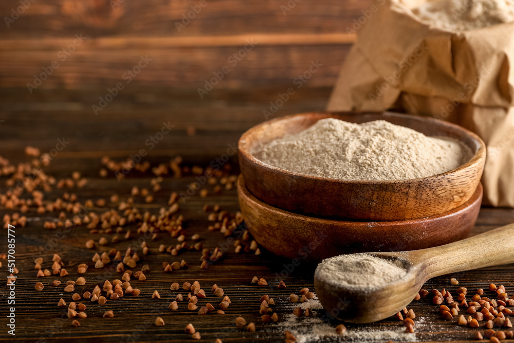 Bowl of flour, spoon and buckwheat grains on dark wooden background