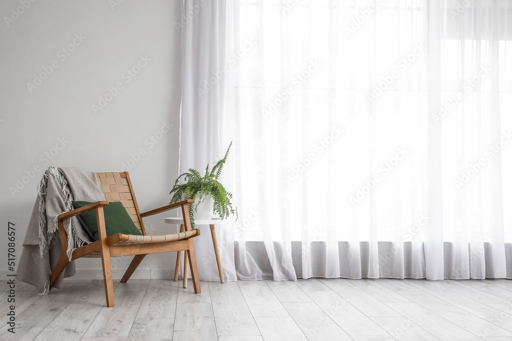 Table with houseplant and armchair near light curtain in room