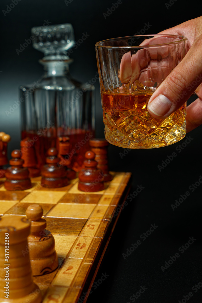 hand holding whiskey in a glass and bottle with chess board