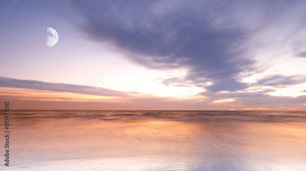 View of the moon rising over the sea with a cloudy sky above the horizon at night. Calm ocean water 