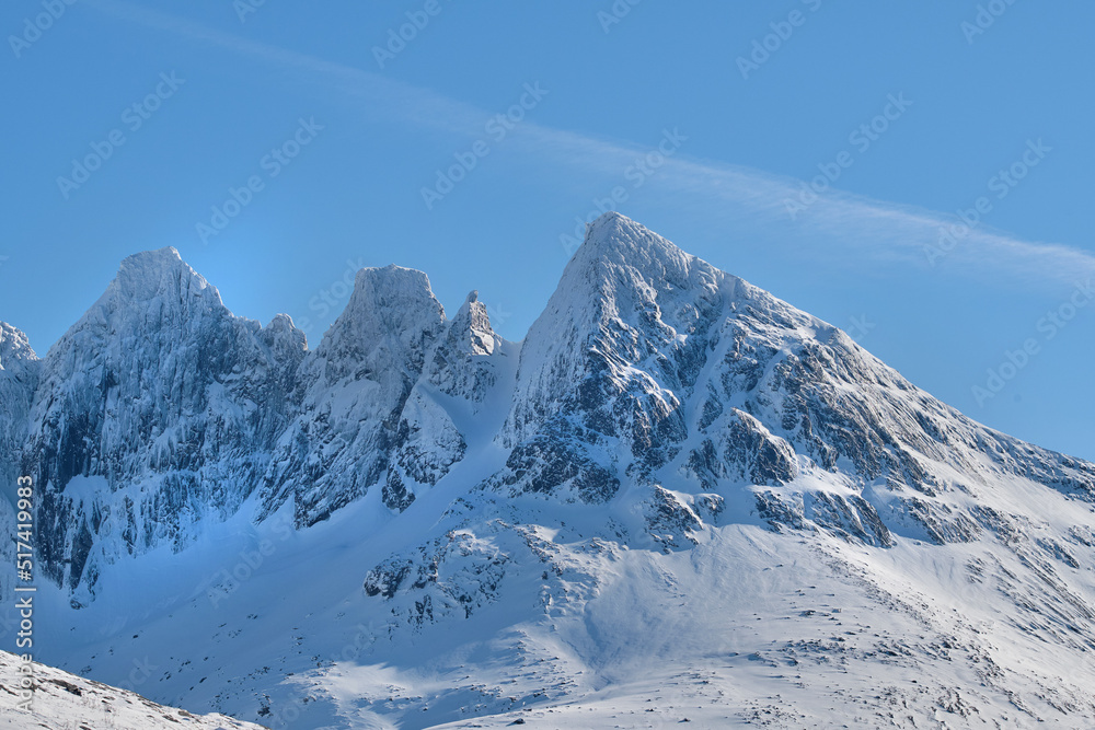 A cold mountain peak covered in snow during winter with a blue sky background. Beautiful landscape o