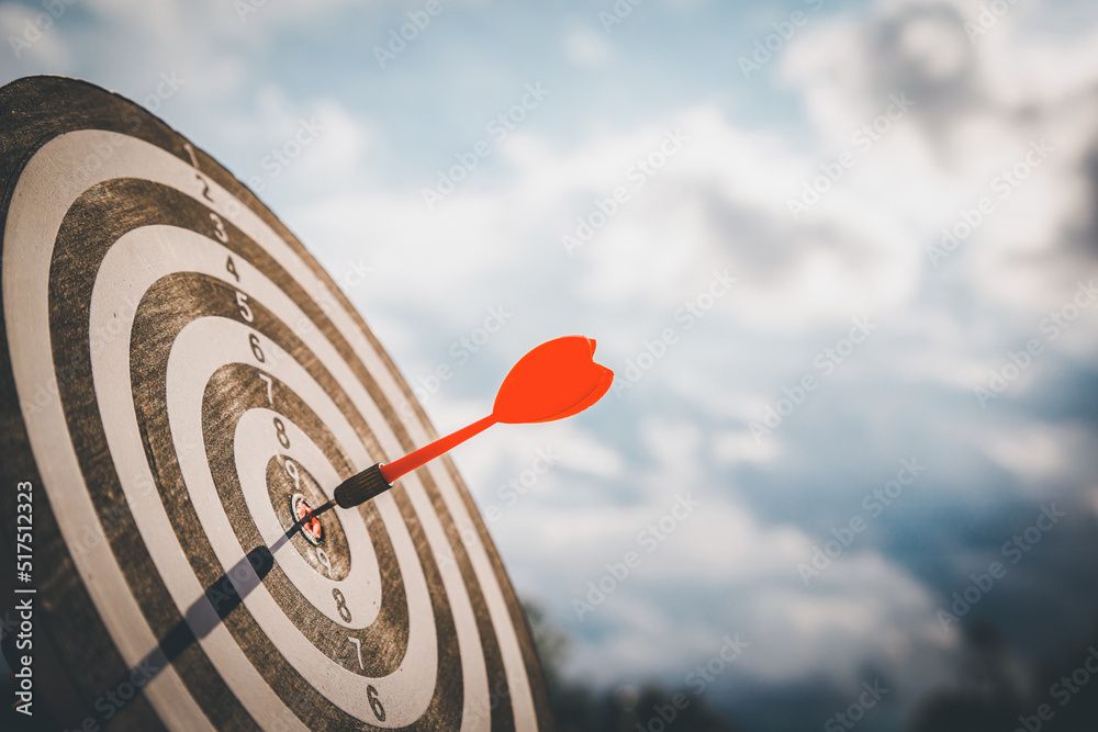 Close up shot red darts arrows in the target  of dartboard center on dark blue sky background. Busin