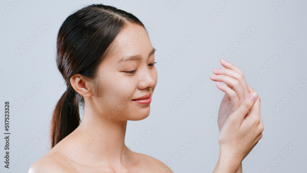 Portrait young asian woman applying hand cream and lotion over grey background