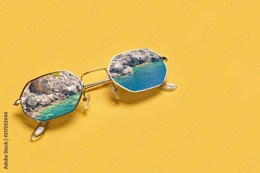 Stylish sunglasses with reflection of sea and mountains on yellow background