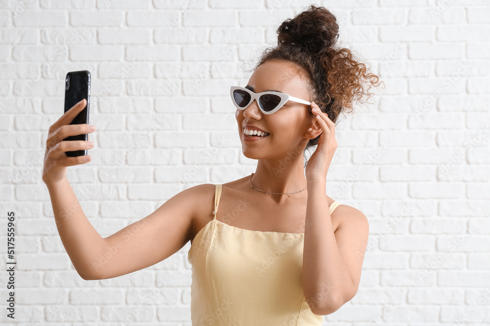 Female African-American tourist taking selfie with mobile phone on white brick background