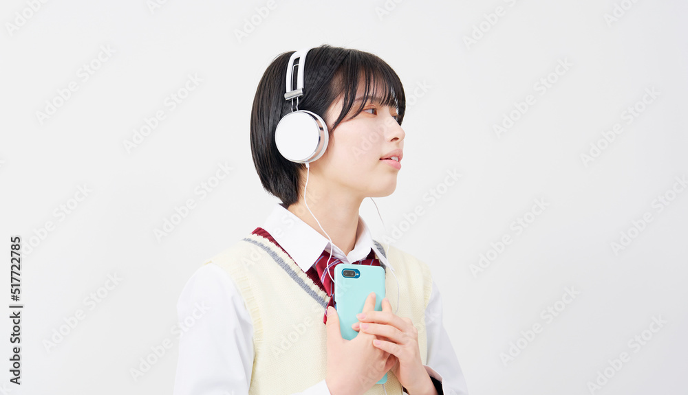 スマートフォンとヘッドフォンで音楽を聴く女子高生　白背景