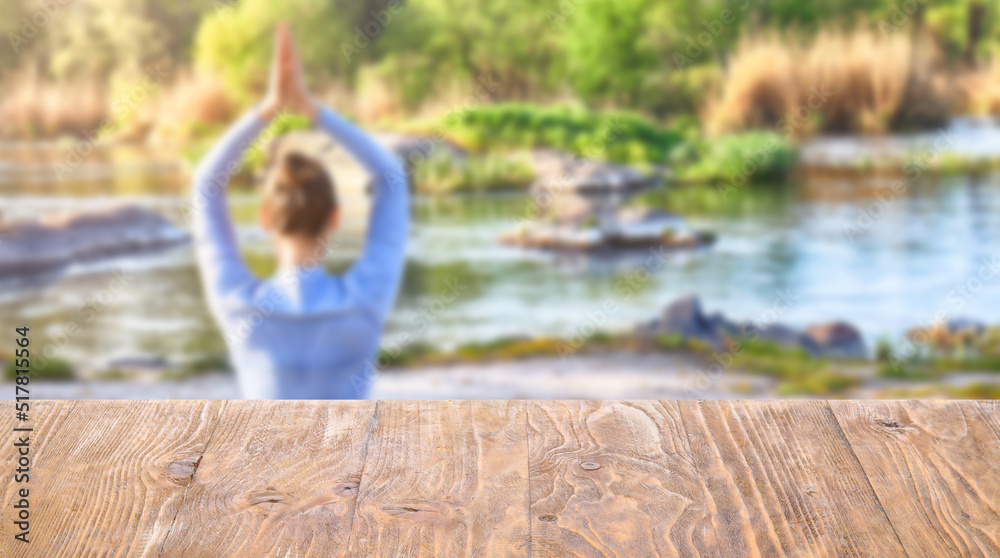 Beautiful young woman practicing yoga near river