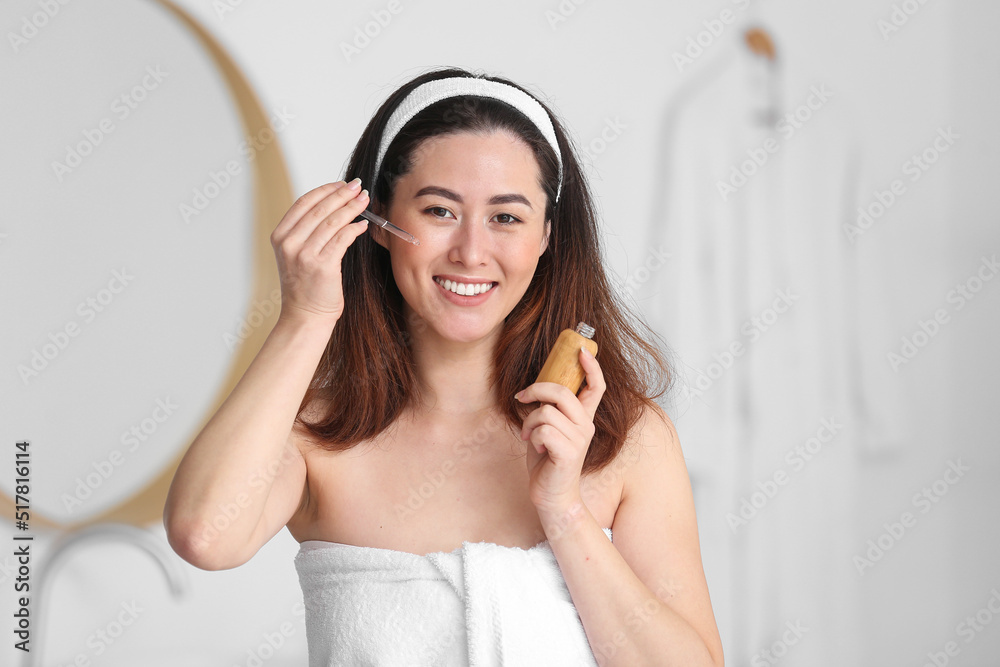 Young Asian woman using cosmetic serum in bathroom