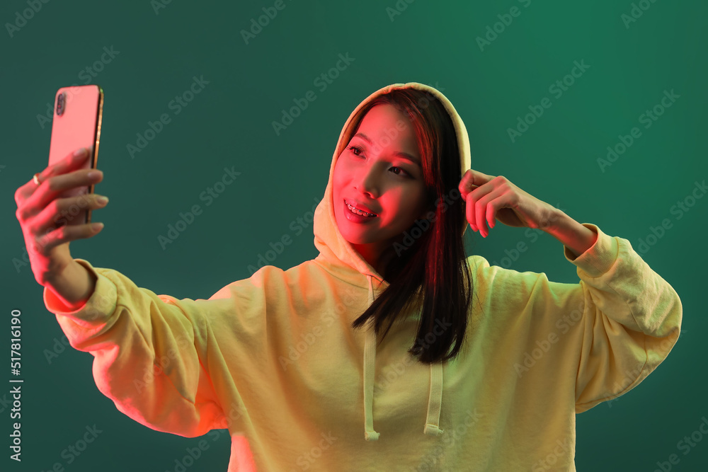 Female Asian blogger with smartphone on green background