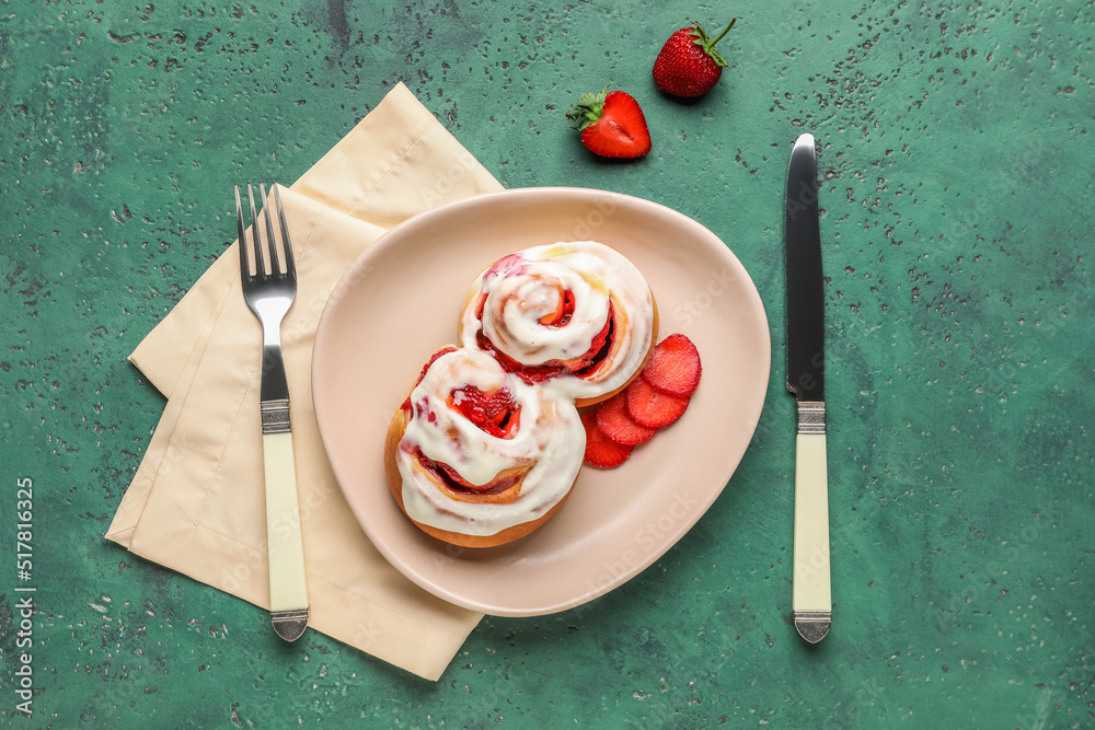 Plate with strawberry cinnamon rolls and cutlery on green background